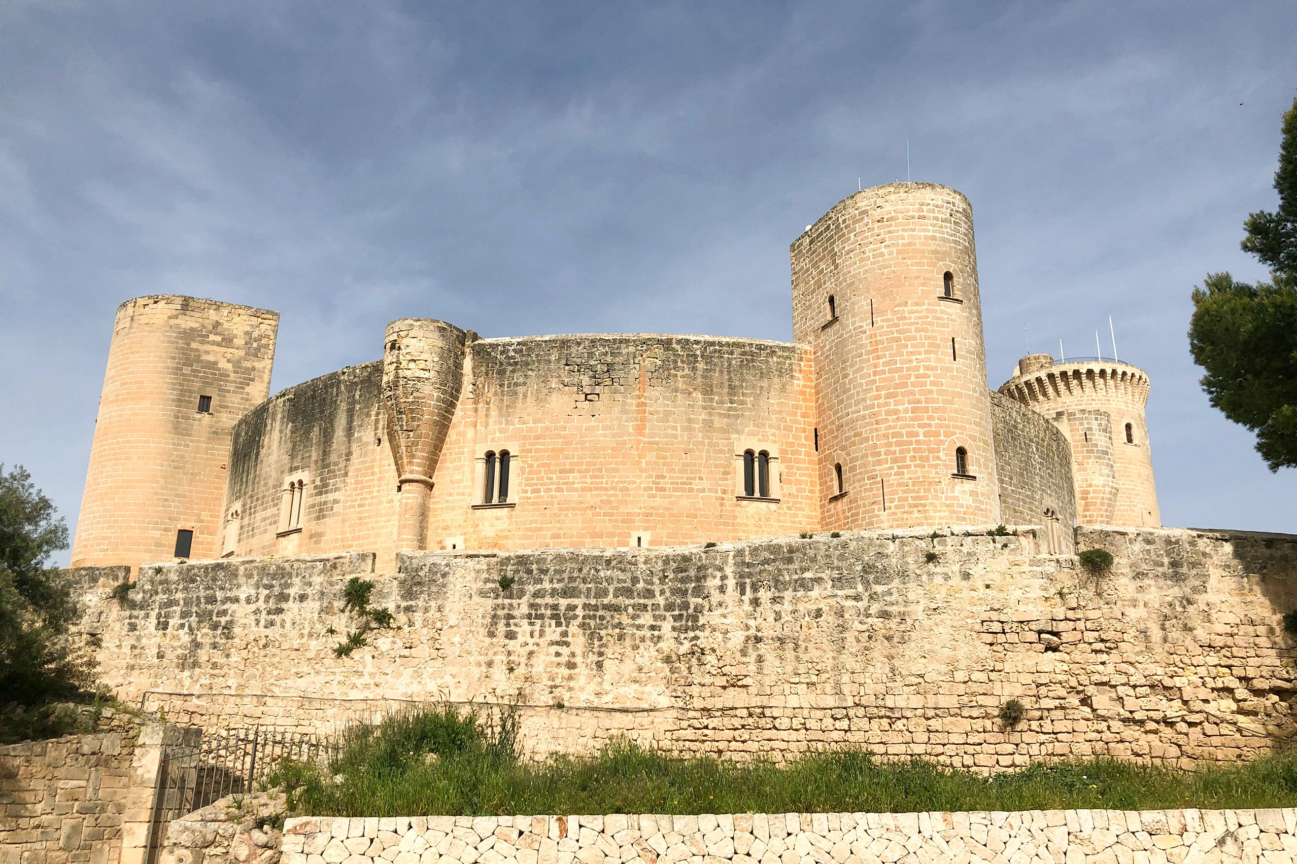 Die runde gotische Burg Castell de Bellver aus hellem Sandstein mit Rundtürmen und umlaufender Mauer auf dem bewaldeten Hügel über Palma.
