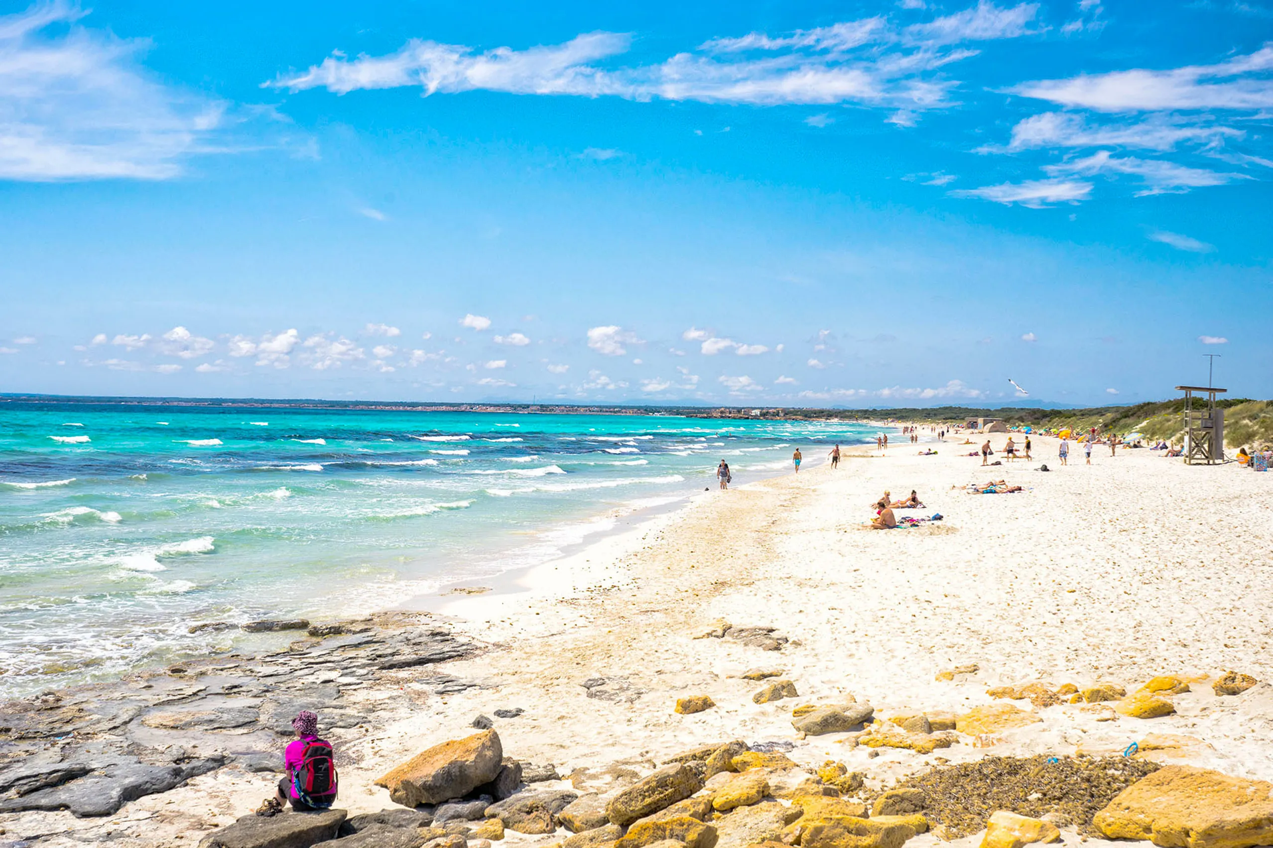 Der Dünenstrand von Es Trenc mit hellem feinem Sand, flachem türkisfarbenem Wasser und niedrigem Bewuchs, ohne jede Bebauung.

