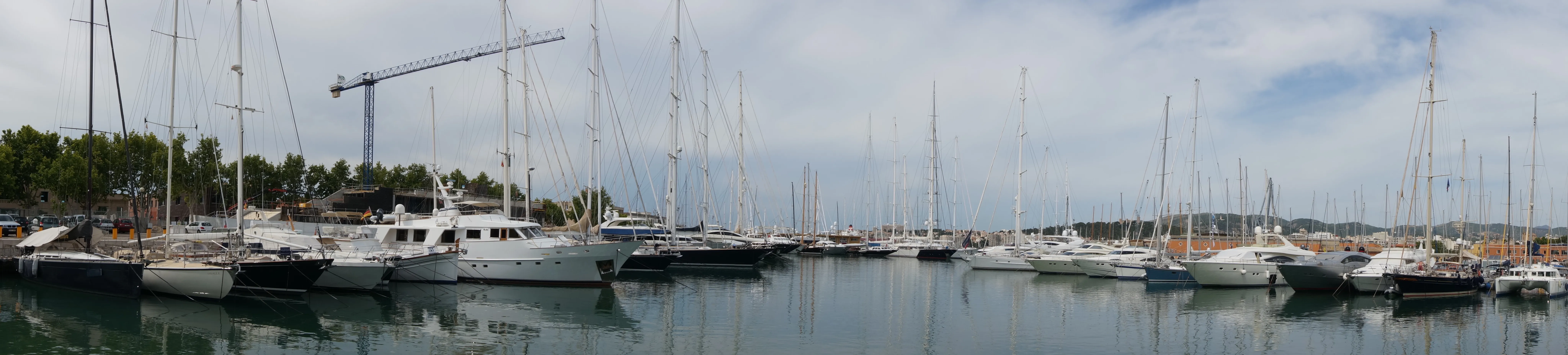 Yachthafen von Palma mit dicht an dicht liegenden Segel- und Motoryachten, im Hintergrund Kräne und die Stadtsilhouette.
