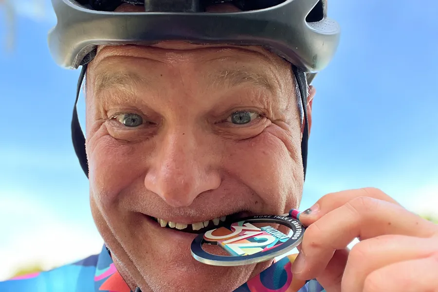 Friedhelm Fischer mit Radhelm beißt lachend in die Finisher-Medaille der Mallorca 312.