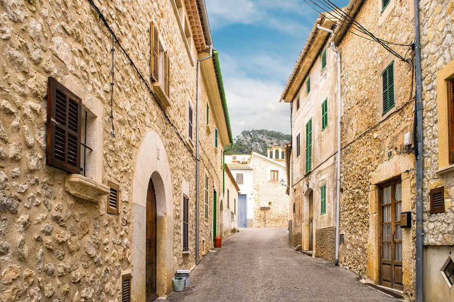 Enge ansteigende Gasse in Caimari zwischen Häusern aus rohem Bruchstein mit Rundbogentoren und grünen Fensterläden.