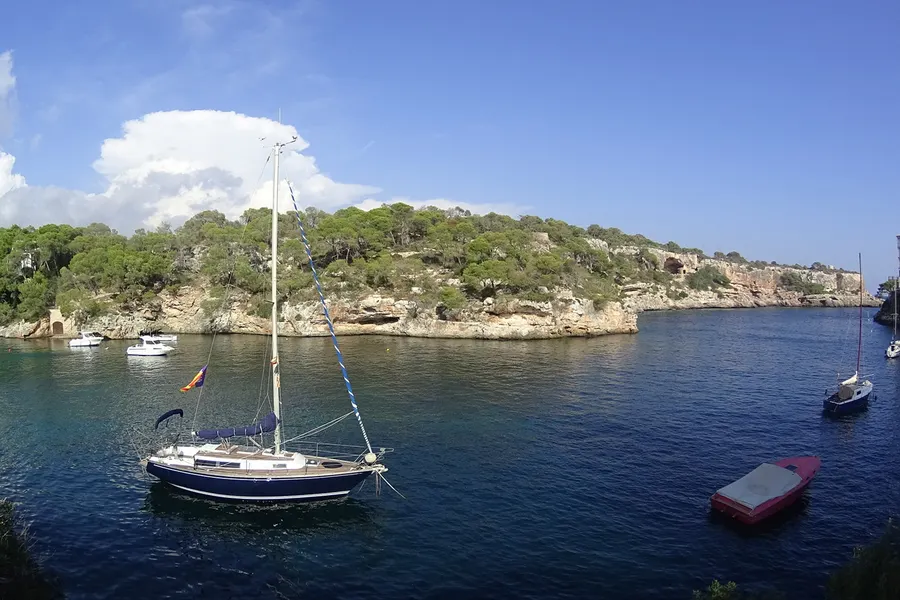 Ankernde Segelboote im ruhigen, tiefblauen Wasser des Einschnitts von Cala Figuera, gerahmt von bewaldeten Felswänden.
