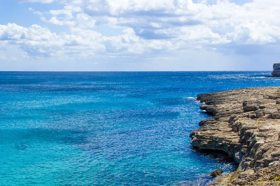 Weite Bucht bei Cala Mondragó mit tiefblauem Wasser, hellen Felsen an beiden Seiten und Kiefernbewuchs auf den Klippen.