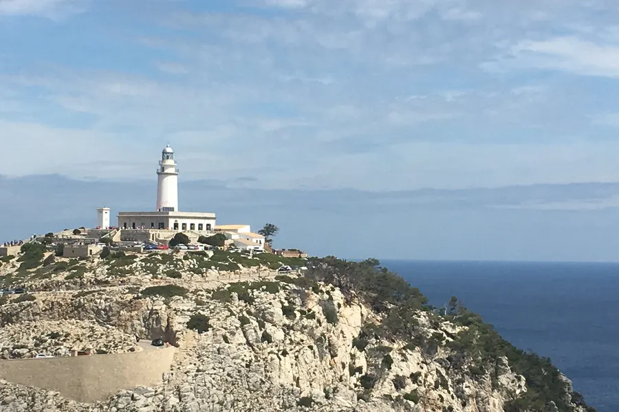 Der Leuchtturm von Formentor mit den umliegenden Gebäuden auf der kahlen Felskuppe, davor die abfallenden Hänge und das Meer.
