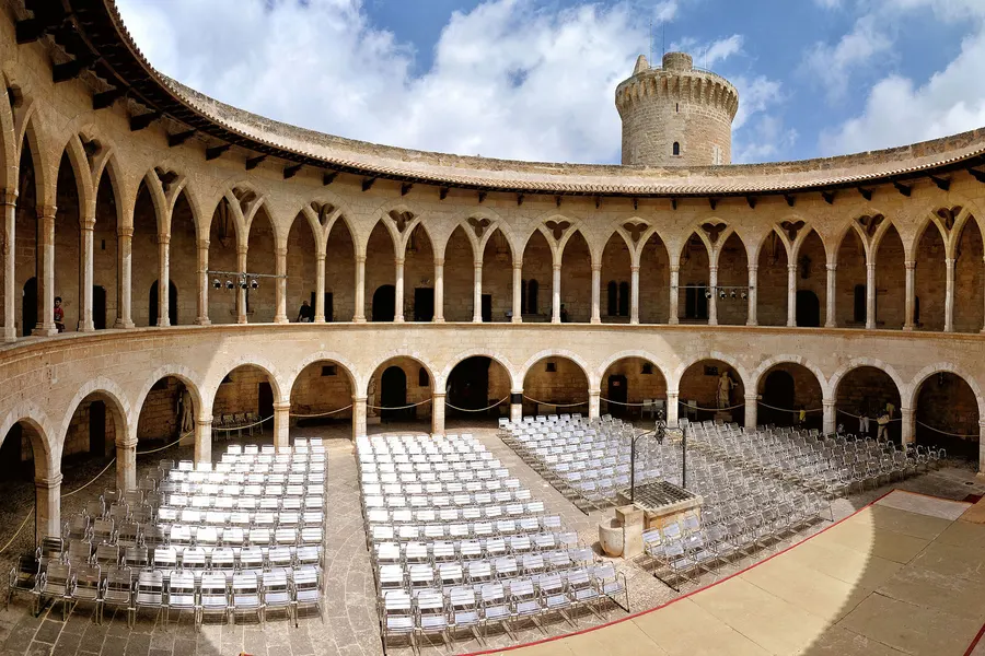 Der zweigeschossige runde Innenhof des Castell de Bellver mit Rundbögen unten und schlanken gotischen Spitzbögen im Obergeschoss, im Hof aufgestellte Stuhlreihen.