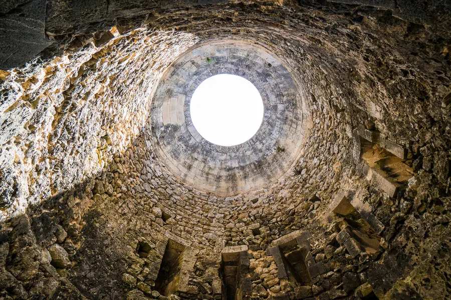 Blick von unten in eine tiefe runde Zisterne des Castell de Santueri, oben die kreisrunde Öffnung zum Himmel.