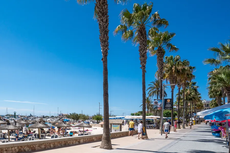 Kleine Badebucht bei Colònia de Sant Jordi mit hellem Sand, flachem türkisfarbenem Wasser und Booten vor der Einfahrt.
