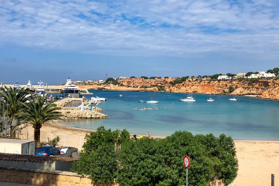 Blick über die Einfahrt zum Hafen Port Adriano mit Molen, Booten und der Bebauung am Ufer, dahinter die Hügel des Südwestens.