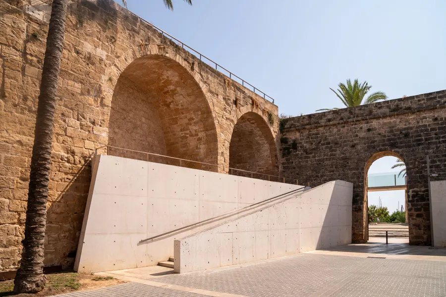 Weiße Betonrampe des Museums Es Baluard, die unter einem alten Steinbogen der Bastion hindurchführt.

