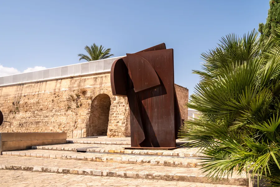 Große Skulptur aus rostrotem Cortenstahl von Rafael Canogar auf dem Vorplatz von Es Baluard in Palma, dahinter Palmen.