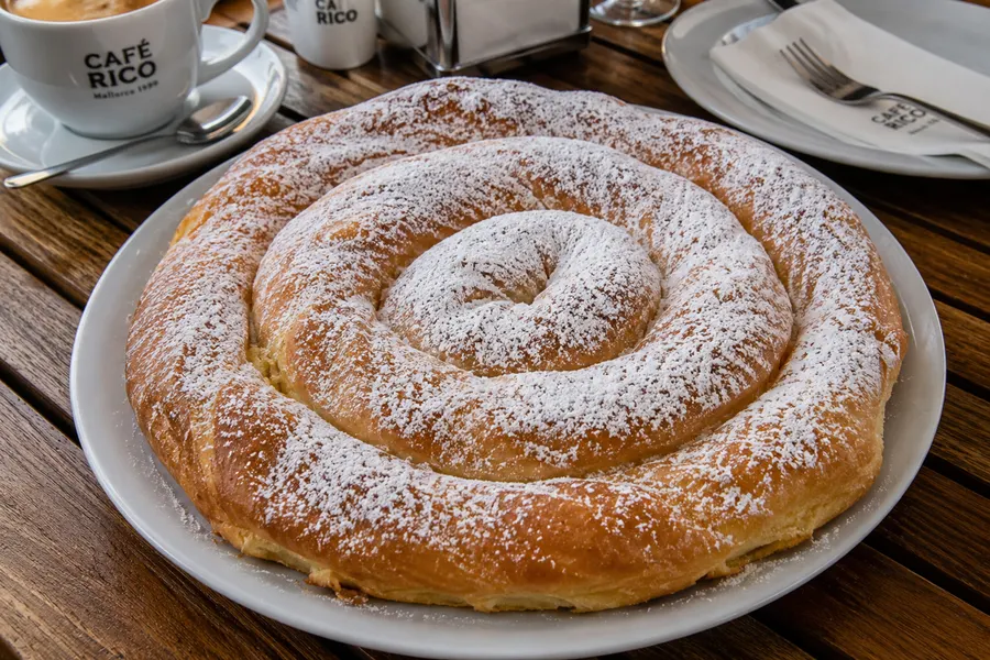 Ensaïmada — Schneckenförmiges Hefegebäck mit Schweineschmalz, mit Puderzucker. (mit künstlicher Intelligenz erzeugte Abbildung)