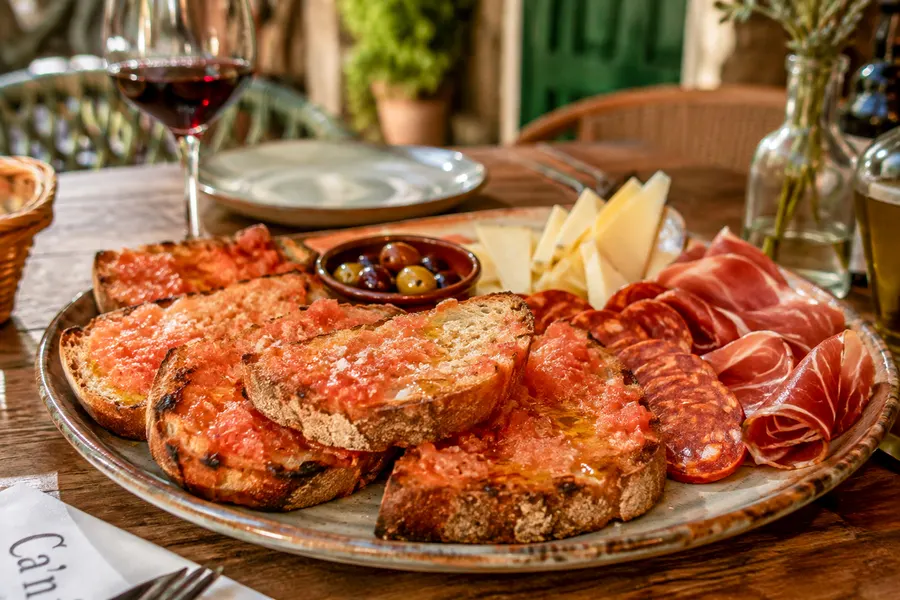 Pa amb oli — Brot, Olivenöl, Tomate, Salz — dazu Käse, Sobrassada oder Schinken. (mit künstlicher Intelligenz erzeugte Abbildung)