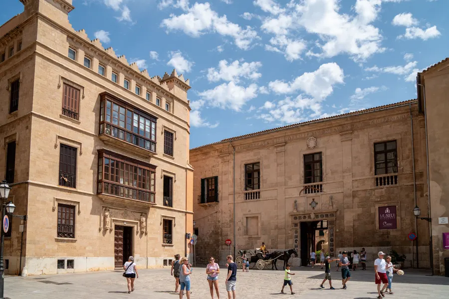 Der Platz vor der Kathedrale von Palma mit dem Bischofspalast, in dem das Diözesanmuseum untergebracht ist, und Passanten.
