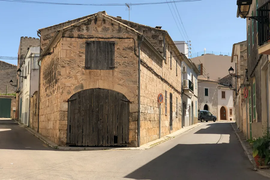 Alter Sandsteinbau mit hohem Rundbogentor an einer schmalen Gasse in Muro, im Hintergrund weiß getünchte Wohnhäuser.
