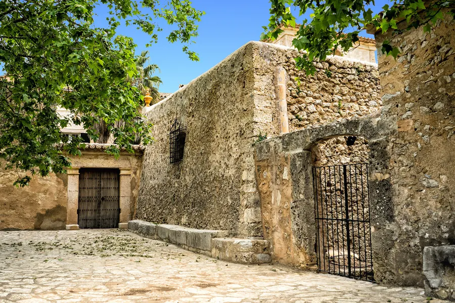 Die kleine Kirche von Orient aus hellem Stein mit Treppenaufgang, daneben eine Trockenmauer und dichtes Grün.