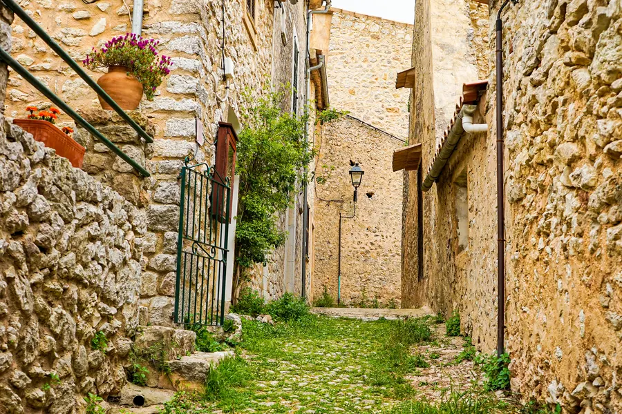 Enge gepflasterte Gasse in Orient mit Stufen zwischen hohen Bruchsteinmauern und einem schmiedeeisernen Geländer.
