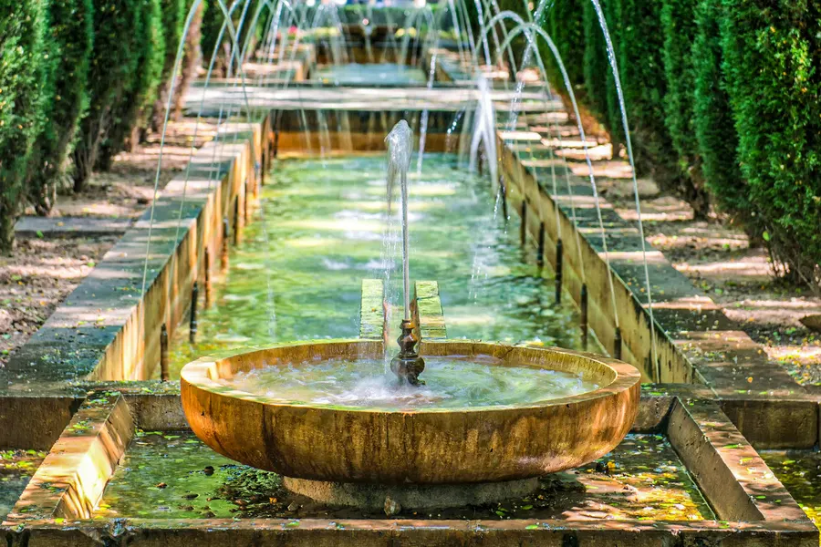 Langer schmaler Wasserlauf mit Springbrunnen und Steinschale im Königsgarten S'Hort del Rei, umgeben von hohen grünen Hecken.
