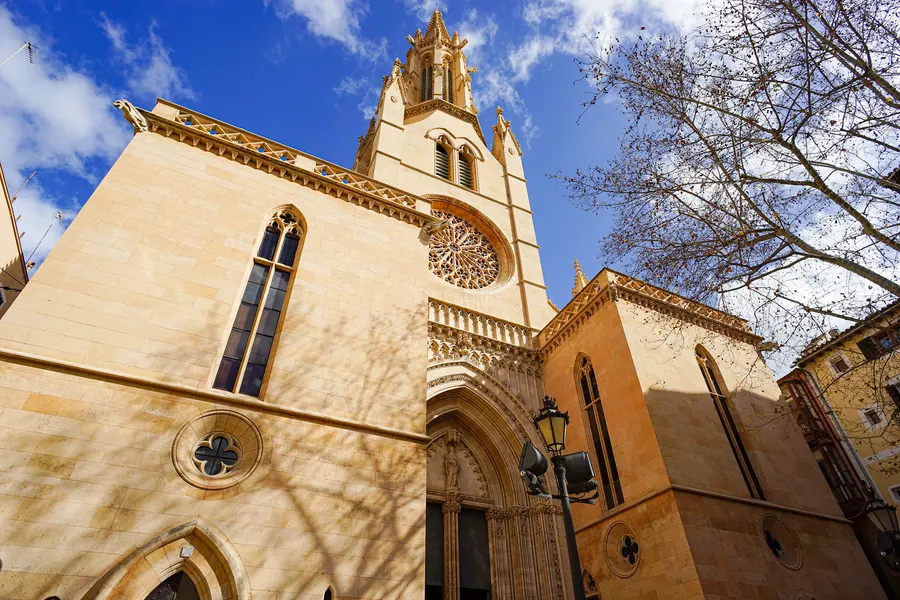 Die gotische Kirche Santa Eulàlia in Palma mit Spitzbogenportal, Rosette und hohem Glockenturm, davor kahle Äste.
