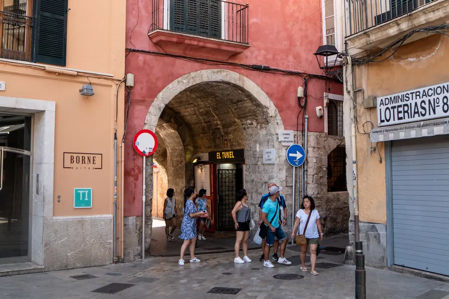 Der überbaute Durchgang El Tunel am Carrer de la Mar in Palma, mit Gewölbe, Straßenschildern und Passanten.
