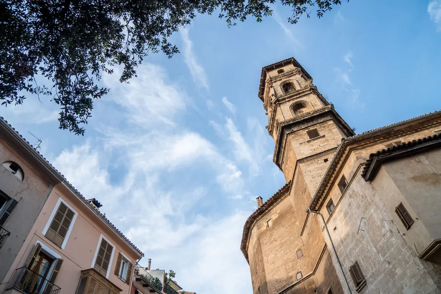 Der Glockenturm und die schlichte Seitenwand der Kirche Sant Nicolau in Palma vor blauem Himmel.
