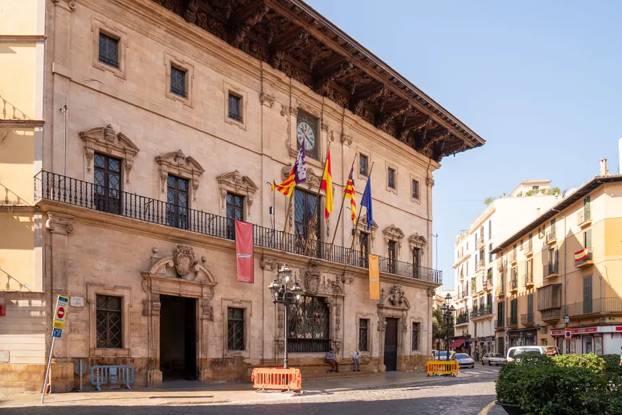 Das Rathaus von Palma an der Plaça de Cort mit Renaissancefassade, Uhr, Balkonen und mehreren Flaggen über dem Portal.