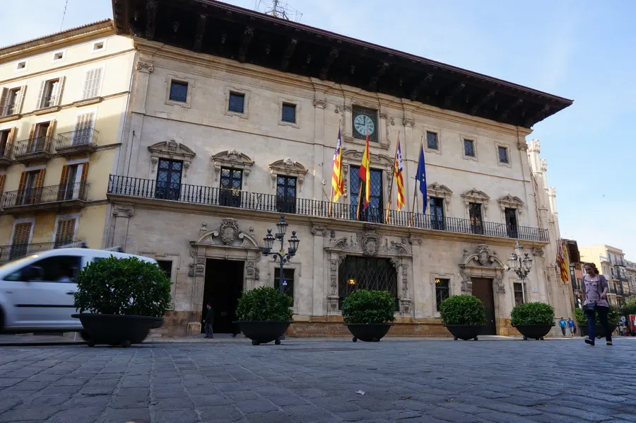 Das Rathaus von Palma an der Plaça de Cort, eine Renaissancefassade mit weit vorkragendem Dachgesims, Uhr und Flaggen.