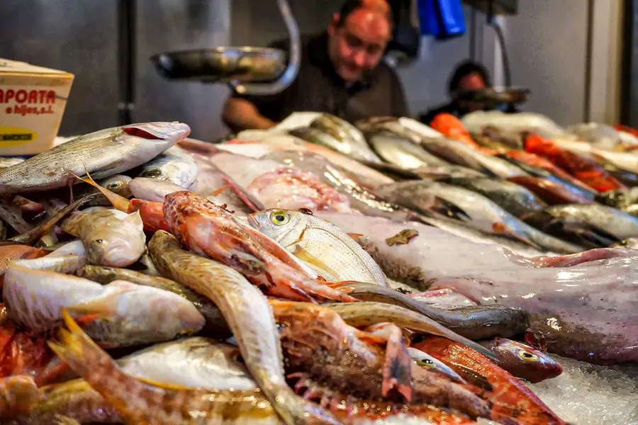 Fischtheke im Mercat de Santa Catalina mit Rotbarben und anderen Mittelmeerfischen auf Eis, dahinter zwei Verkäufer.
