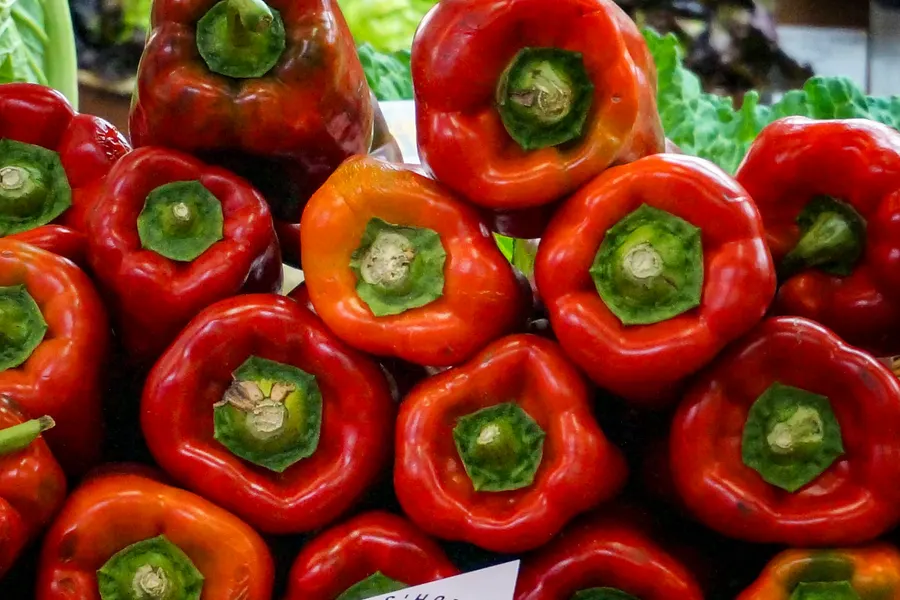 Gestapelte rote und orangefarbene Paprikaschoten an einem Gemüsestand des Mercat de Santa Catalina.
