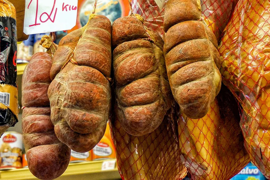 Mehrere Stränge Sobrassada in orangefarbenen Netzen an einem Stand in der Markthalle.
