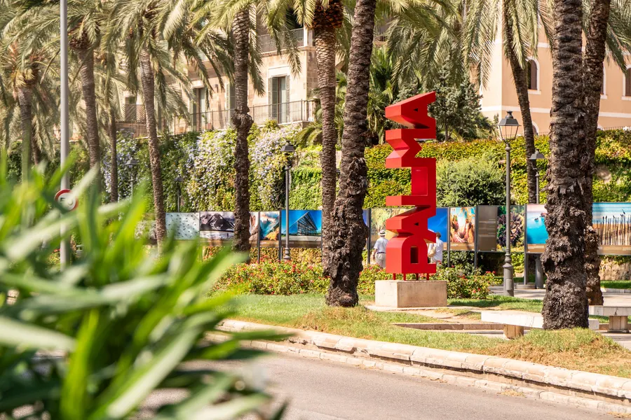 Roter Schriftzug PALMA als Skulptur zwischen Palmen an einer Grünanlage in Palma.

