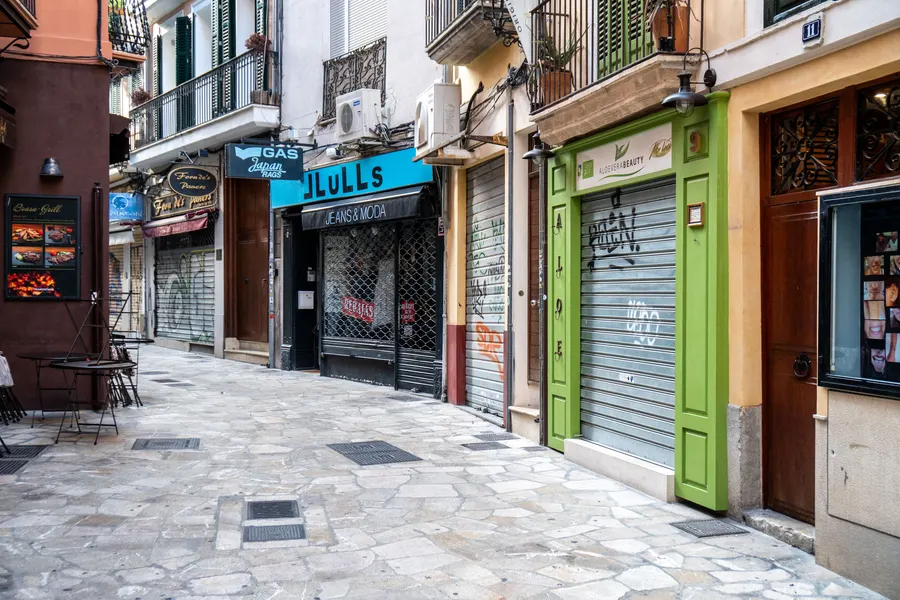 Eine Einkaufsgasse in Palma am frühen Morgen mit heruntergelassenen Rollläden und leerem Pflaster.
