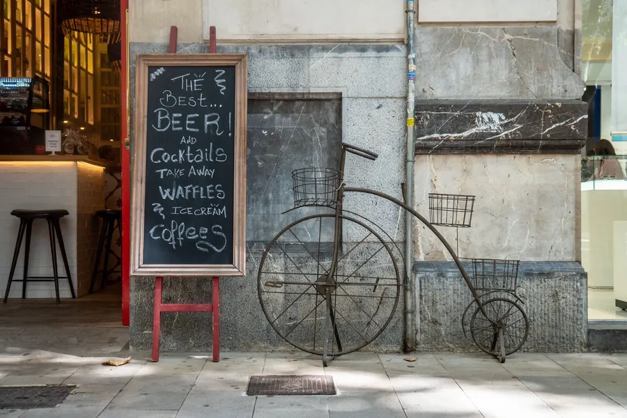 Fassade eines Cafés in Palma mit Kreidetafel und einem alten Hochrad als Dekoration an der Wand.
