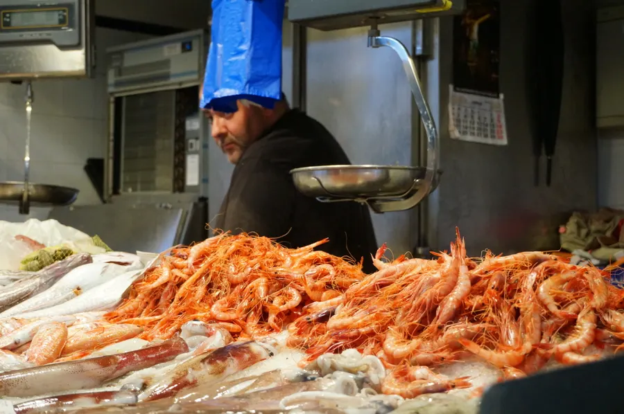 Fischstand in einer Markthalle in Palma, große Mengen frischer Garnelen auf Eis, dahinter ein Händler bei der Arbeit.