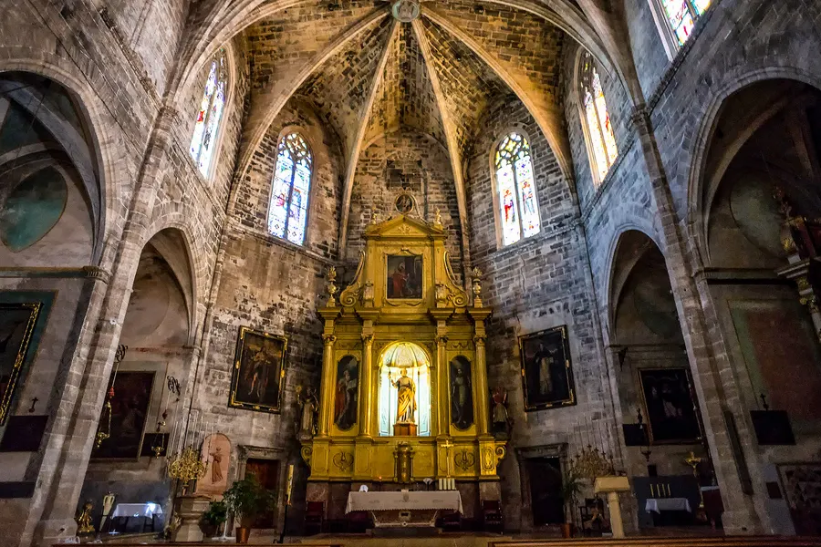 Das Innere der Pfarrkirche von Petra mit hohem Kreuzrippengewölbe, Seitenkapellen und einem vergoldeten Barockaltar im Chor.