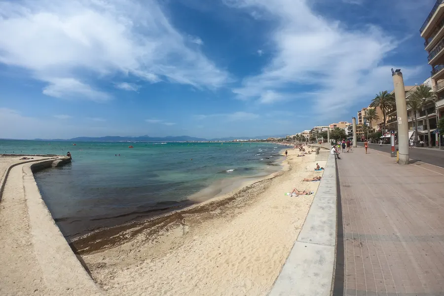 Drei geöffnete Sonnenschirme und Liegen am leeren Sandstrand der Platja de Palma, davor das ruhige Meer.
