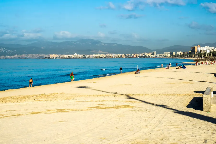 Blick über den hellen Sandstrand und das blaue Wasser der Platja de Palma in Richtung der Stadt und der Tramuntana.
