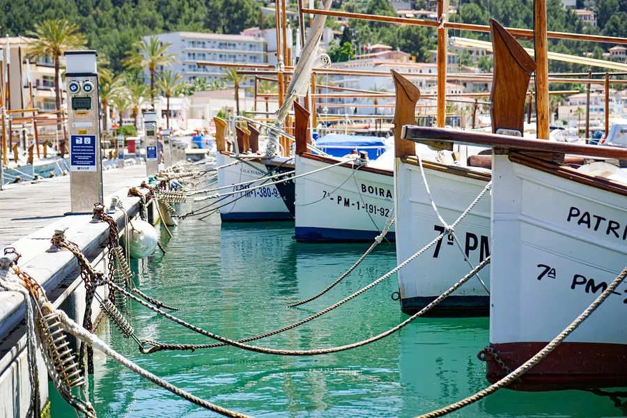 Heller Sandstrand von Port de Sóller mit ruhigem türkisfarbenem Wasser, dahinter die Bebauung am Hang und die Berge.
