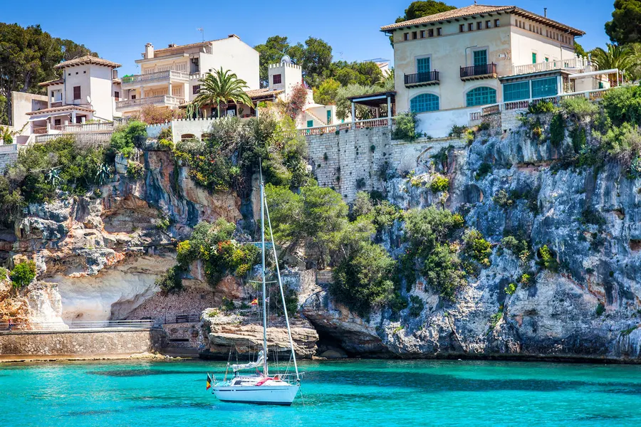 Blick über die schmale Bucht von Porto Cristo mit einem ankernden Segelboot im türkisfarbenen Wasser, gerahmt von felsigen, bewachsenen Ufern.
