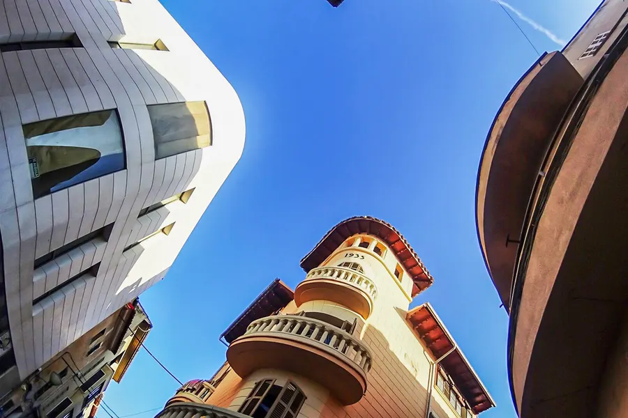 Steil nach oben fotografierter Eckturm eines Wohnhauses in sa Pobla mit umlaufenden Balkonen und Ziegeldach, daneben eine moderne weiße Fassade.
