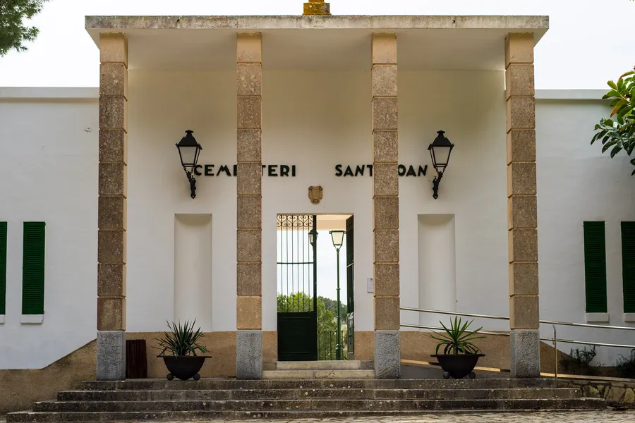 Weiß verputzter Eingangsbau des Friedhofs von Sant Joan mit Säulen, schmiedeeisernem Tor und der Aufschrift Cementeri Sant Joan.
