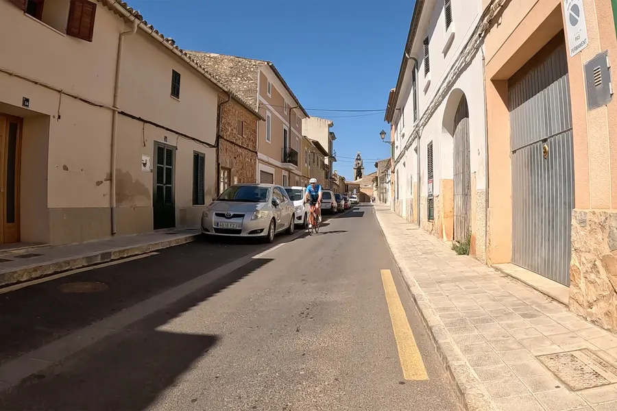 Kreuzung in Santa Maria del Camí mit Bruchsteinhäusern, einem Stoppschild auf der Fahrbahn und leeren Gehwegen.
