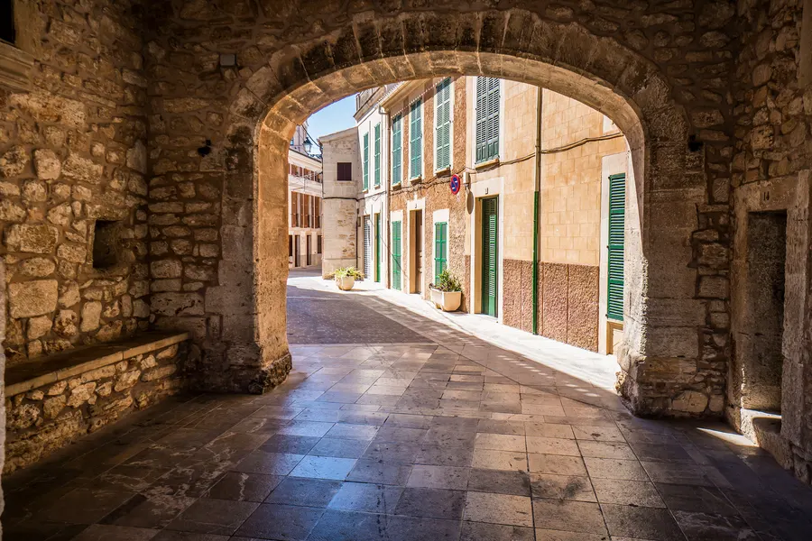 Blick durch den Torbogen der Porta Murada in Santanyí auf die dahinter liegende Gasse mit hellen Häusern und blauen Fensterläden.