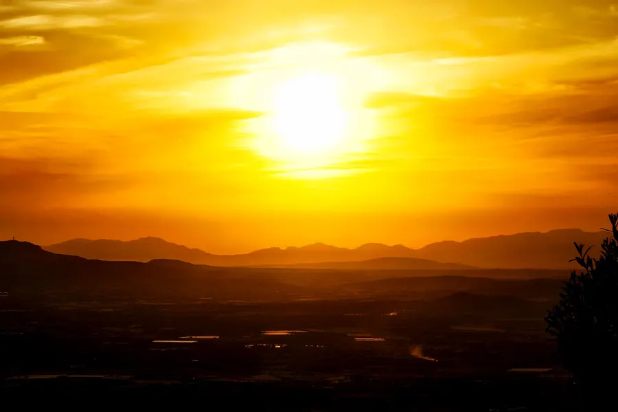 Sonnenuntergang über der Ebene, vom Gipfel bei Sant Salvador aus gesehen, mit Bergsilhouetten im Gegenlicht.
