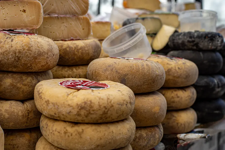 Gestapelte Laibe mallorquinischen Schafskäses mit Kräuterrinde an einem Marktstand in Sineu.