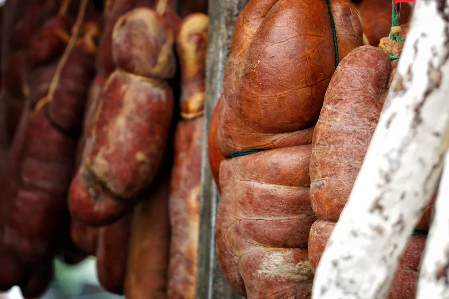 An Schnüren hängende Sobrassada- und Wurstwaren in kräftigem Rot an einem Marktstand in Sineu.
