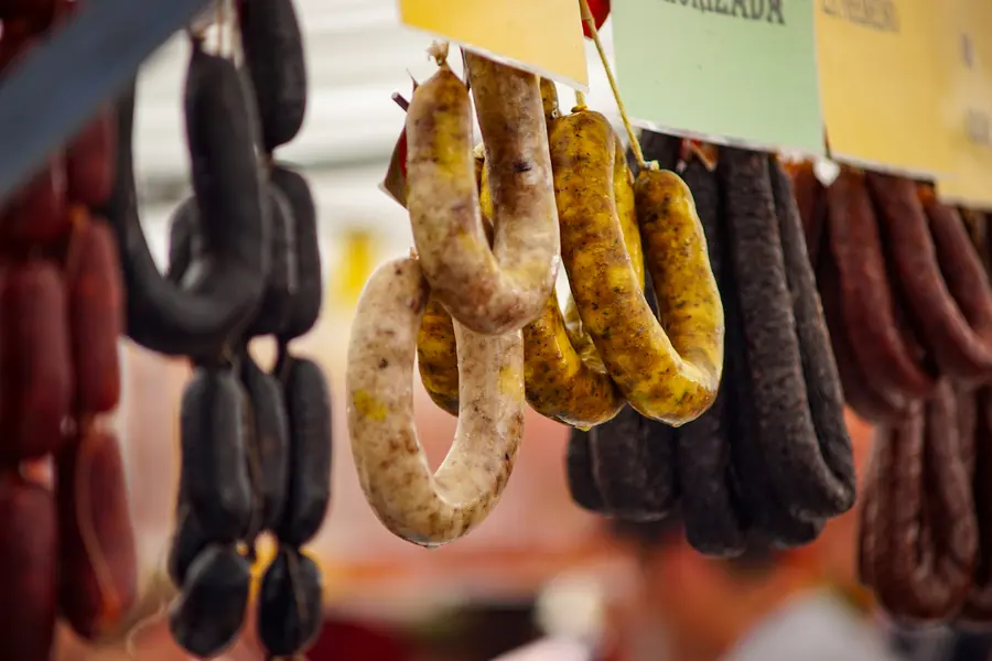 Ringe geräucherter und heller Wurst hängen dicht nebeneinander an Haken über einem Marktstand.