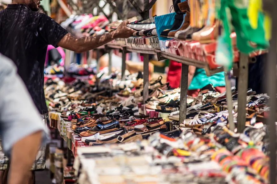 Schuhe in Reihen auf einem Markttisch ausgelegt, dahinter weitere Kisten und Ware.